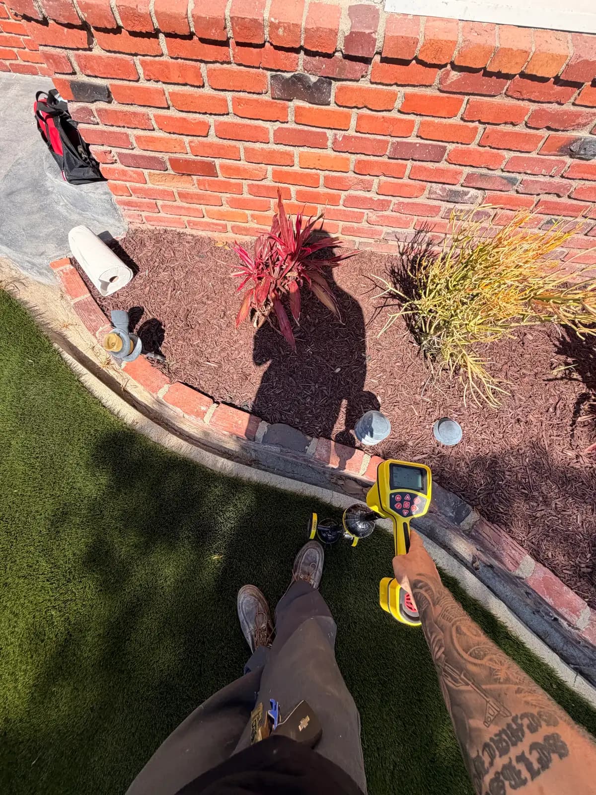 Mainline Plumbing technician using a yellow-handled pipe locator wand to pinpoint the camera sonde and mark the exact location and depth of a sewer defect on the ground