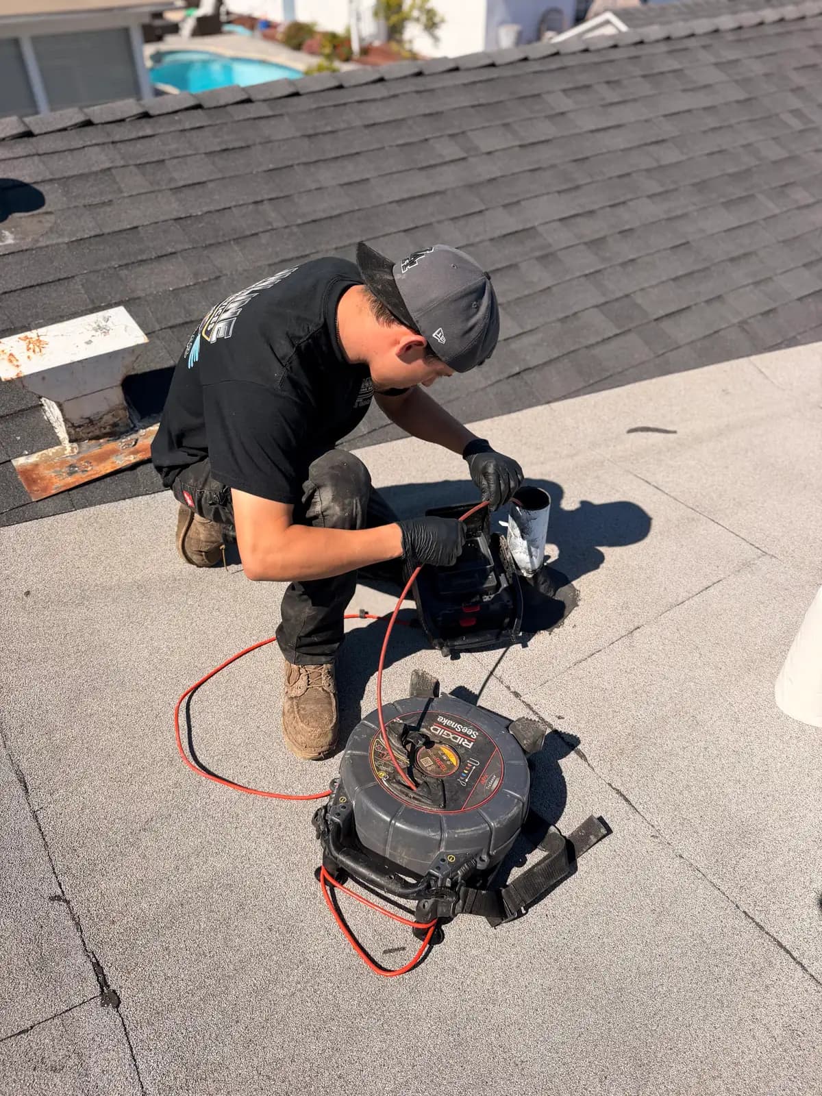 Mainline Plumbing technician feeding a self-leveling sewer inspection camera down a rooftop vent stack on a South Bay home to record the drain line in real time