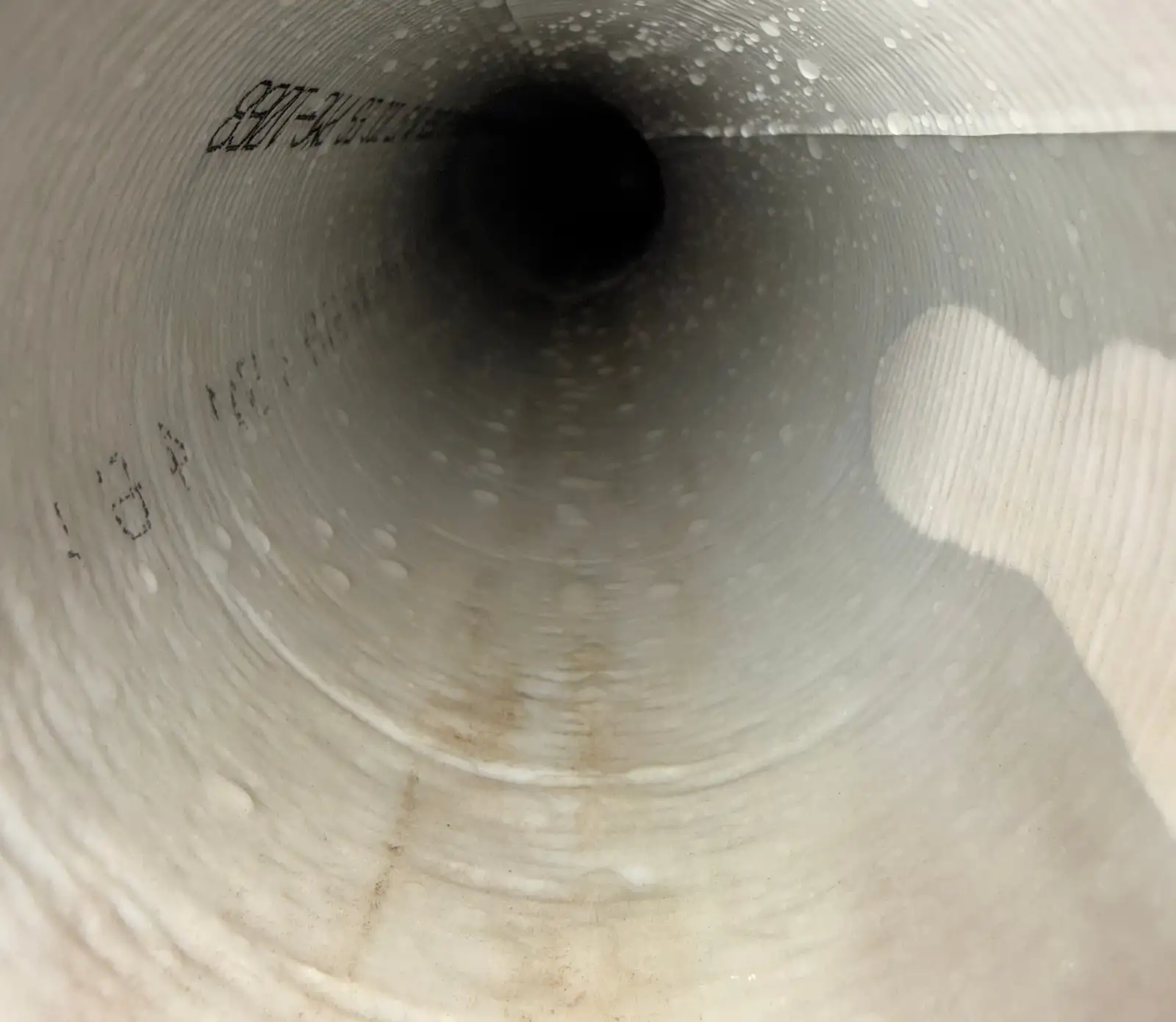View down the inside of a freshly cured CIPP sewer liner showing a smooth white continuous wall with the manufacturer's printed markings