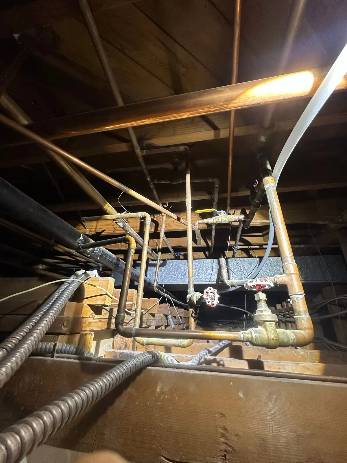 New copper water distribution lines with gate valves run overhead through a subfloor crawlspace during a Mainline Plumbing repipe