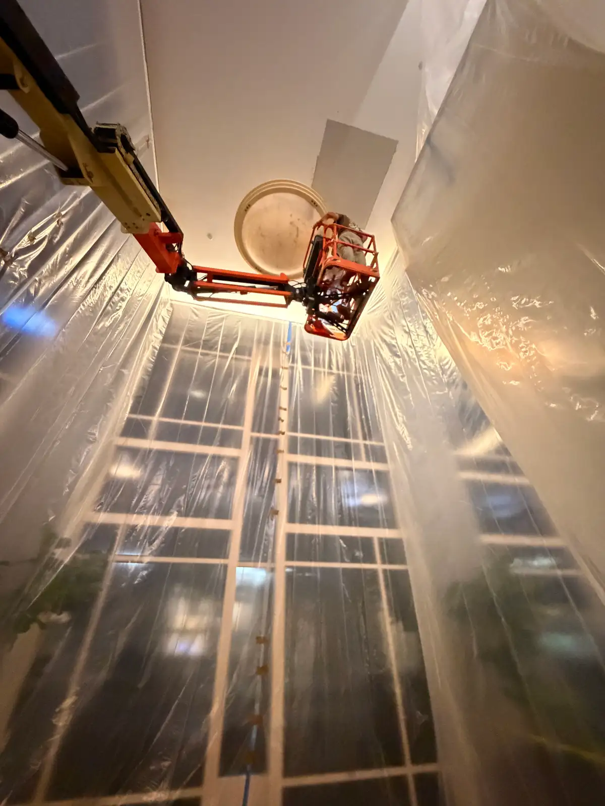 Mainline Plumbing overnight commercial job at Providence St. Joseph Hospital in Orange — boom lift and floor-to-ceiling plastic containment drapes sealing a high atrium work zone