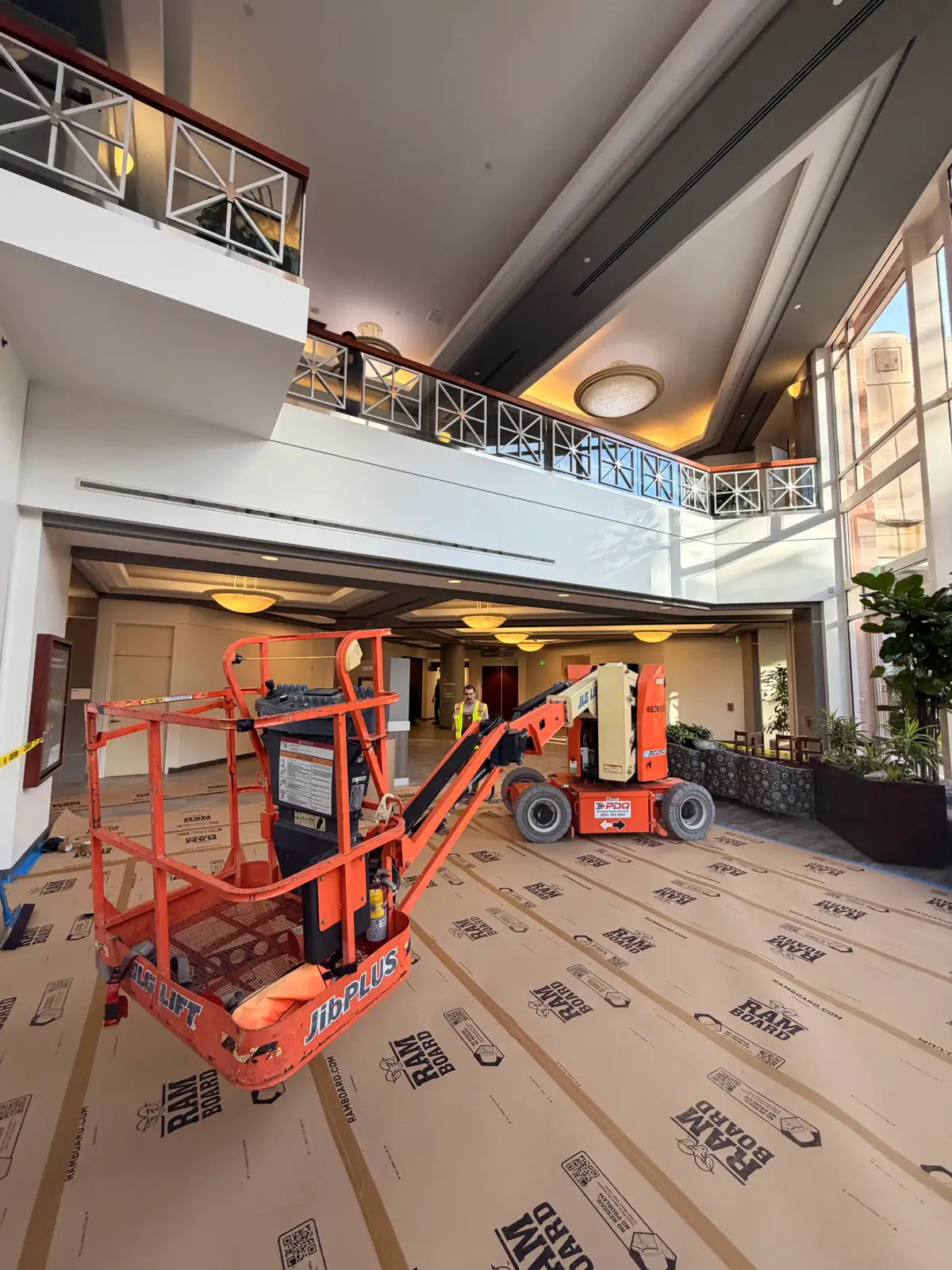 Articulating boom lift positioned in a hospital atrium with RAM BOARD wall protection during a Mainline Plumbing commercial cast iron replacement