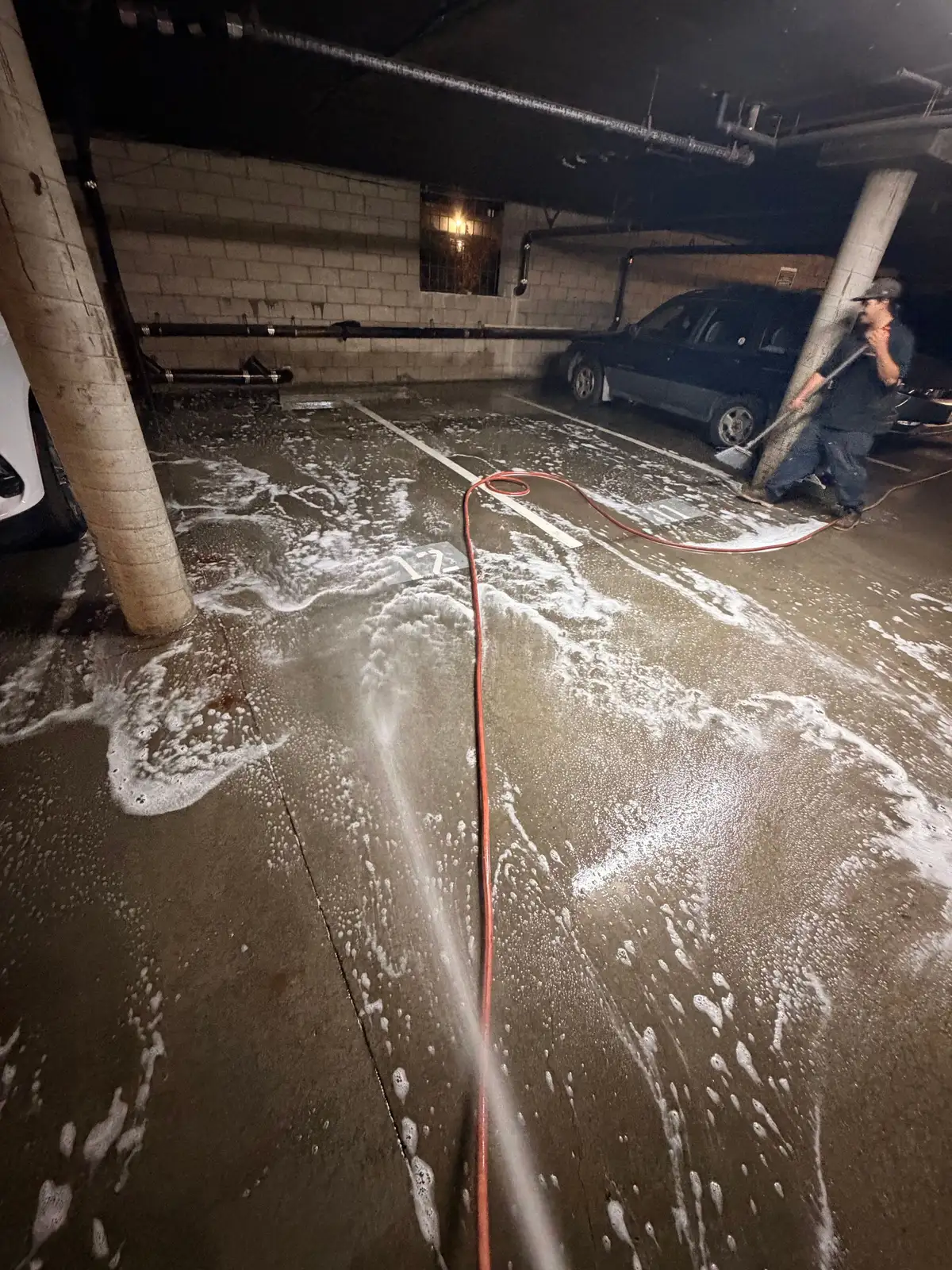 Mainline Plumbing technician pressure washing and squeegeeing a subterranean parking garage floor after clearing a commercial sewage backup