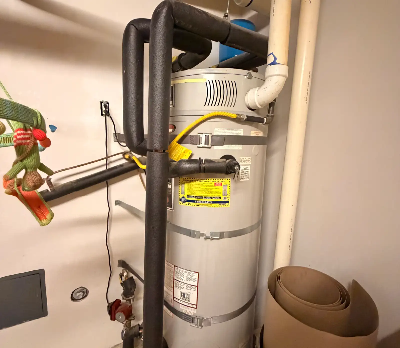 Newly installed gas storage water heater in an interior closet with two seismic straps bolted to the framing at the upper and lower thirds of the tank, insulated hot and cold lines, a corrugated gas connector, and a thermal expansion tank mounted on the line above