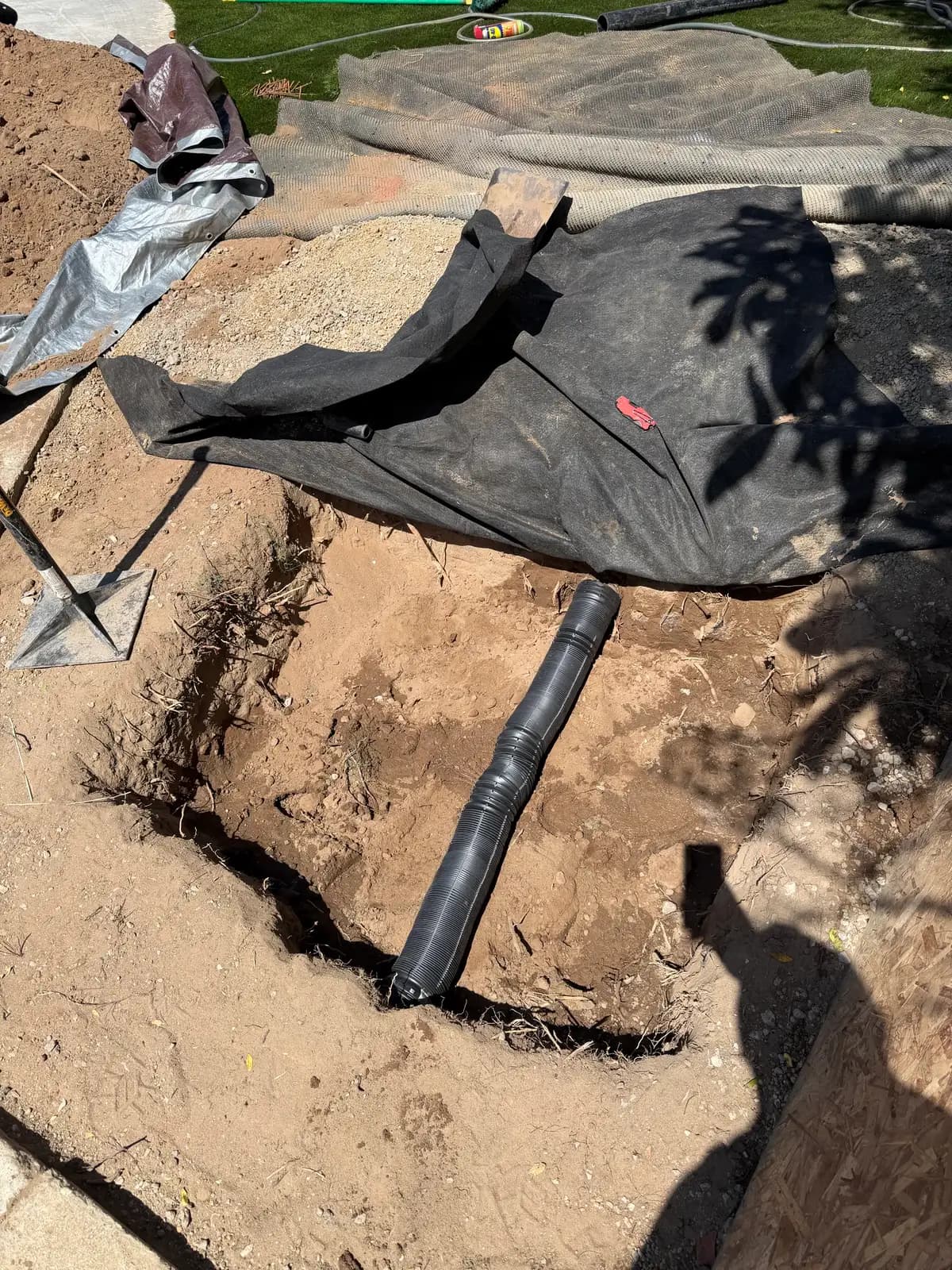 Ground protection fabric laid over the lawn beside a narrow trench as new HDPE sewer pipe is fed in
